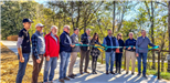 People holding a ribbon and cutting it in front of a walking trail. 