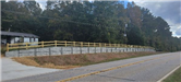 Concrete walking path between a retaining wall and a metal fence next to a road. 