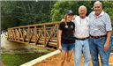 Three people standing in front of an iron bridge. 