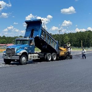 Dump truck emptying asphalt. 3 men working alongside the paving truck. 