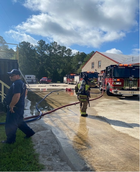 One firefighter in full gear and one in day clothes 3 fire trucks & ambulance