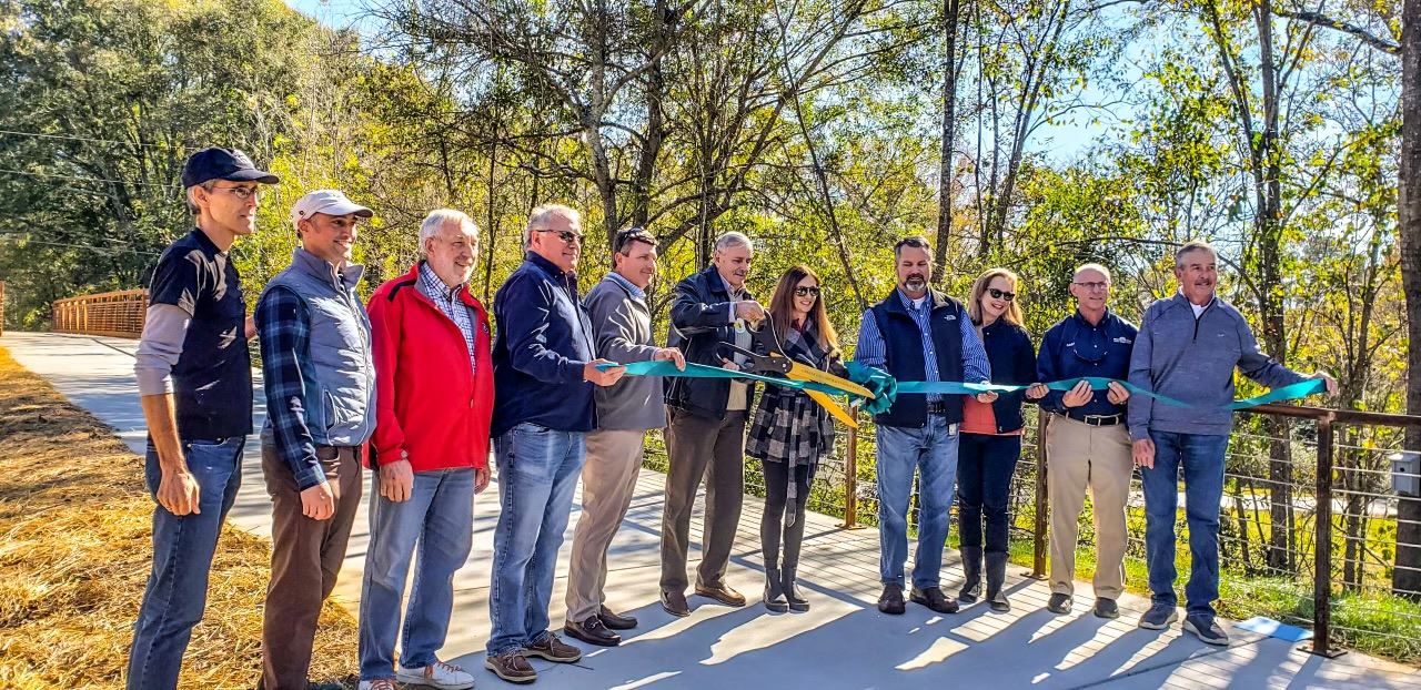 People holding a ribbon and cutting it in front of a walking trail. 
