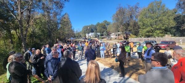 Group of people standing on a concrete walking path listening to a speaker