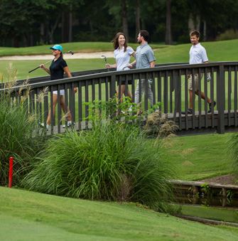 Two couples walking over a bridge carrying clubs at the golf course